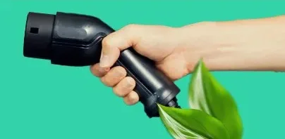 Hand holding an electric vehicle charging connector with green leaves